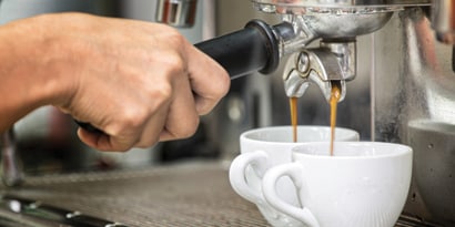 Espresso being dispensed into two white shot mugs from commercial espresso machine