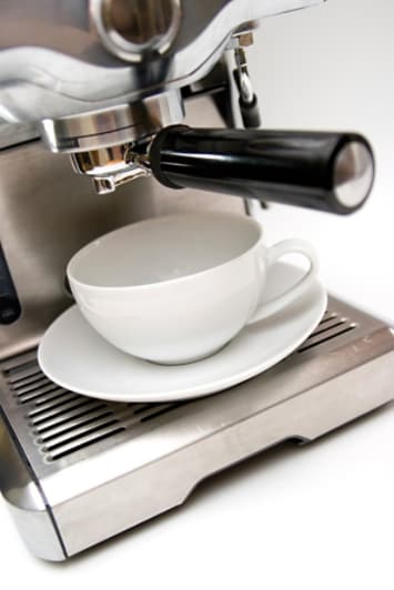 Espresso machine ready to dispense into white mug and saucer