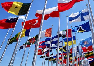 A diverse array of national flags from various countries are flying on flagpoles against a clear blue sky.