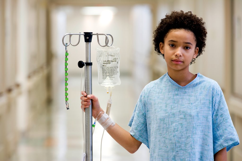 Young child standing in a hospital gown with an IV drip