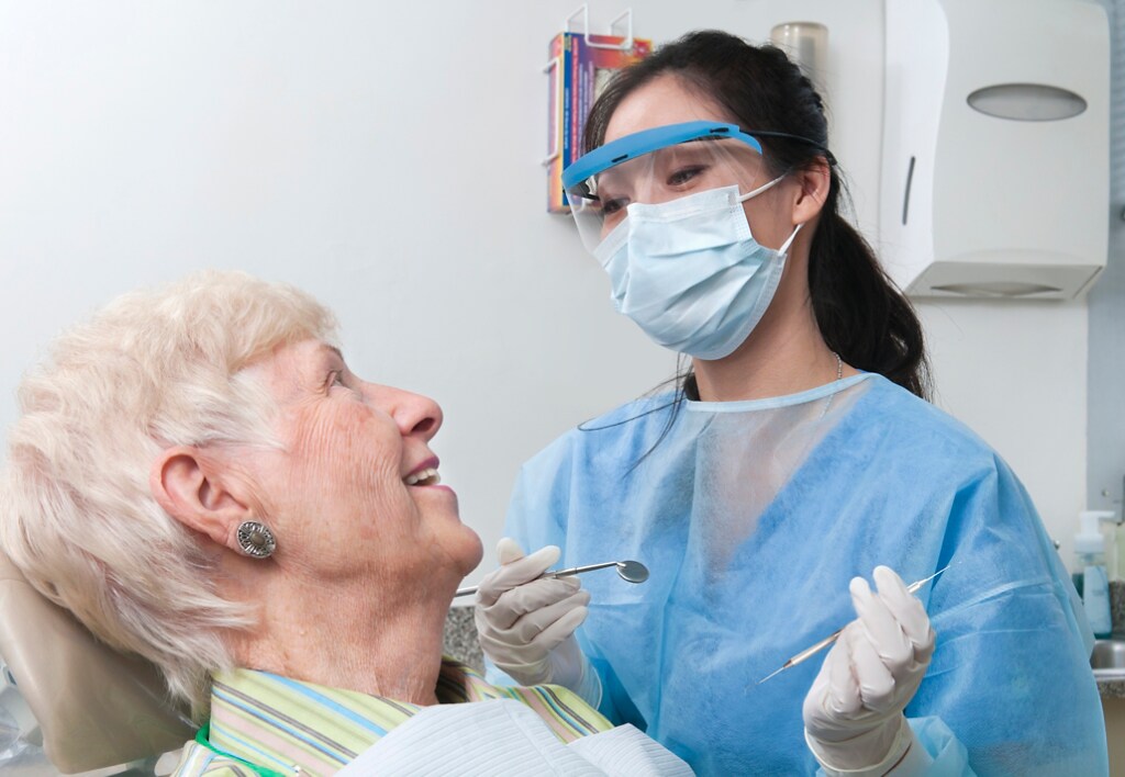 Dentist wearing PPE treating elderly woman 