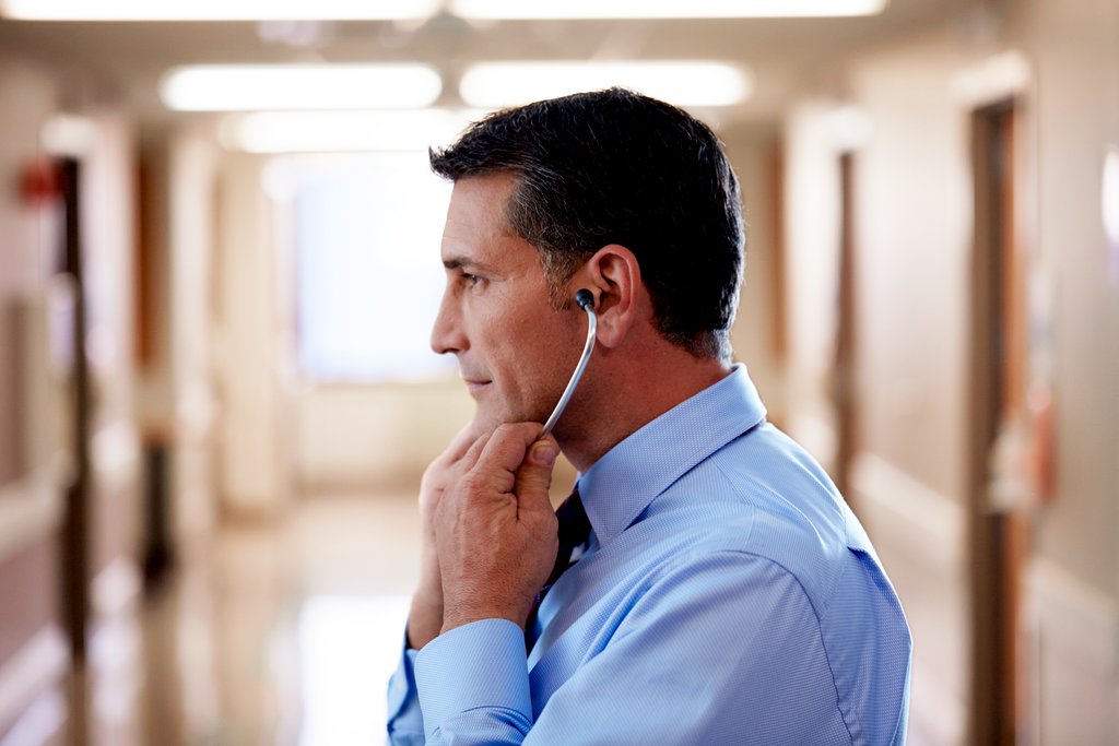 Male doctor in a blue dress shirt putting on a Littmann Cardiology IV Diagnostic Stethoscope.  