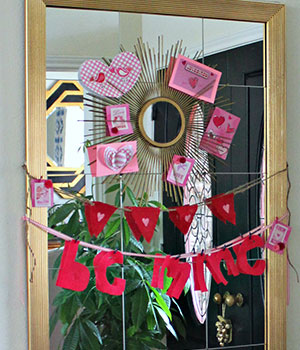 sunburst mirror with valentines day decor stuck on larger mirror using Command strips with hanging garland below