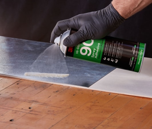 Image of a worker spraying adhesive on a metal sheet