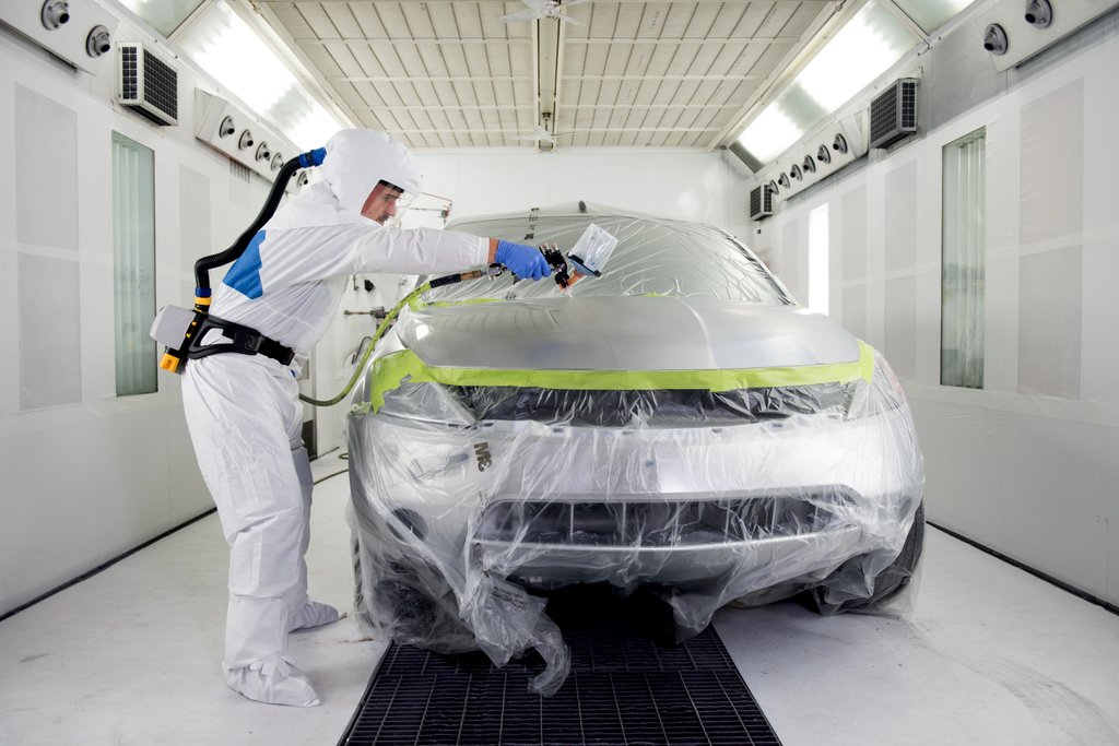 Two workers wearing powered air-purifying respirators review a clipboard in an industrial workspace, with on-screen text about a passive speaking diaphragm for communication.