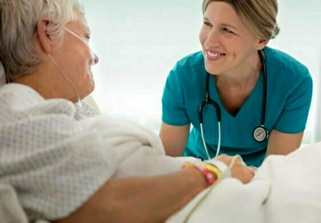 female doctor taking the hand of an older patient who is in a hospital bed 