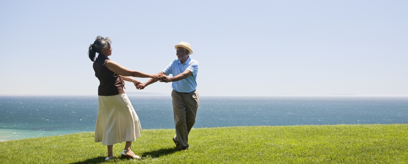 Senior couple holding hands and spinning on grassy hill overlooking ocean