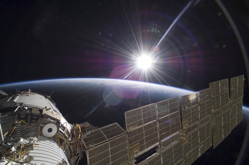 The International Space Station backdropped by the bright Sun over Earth's horizon.