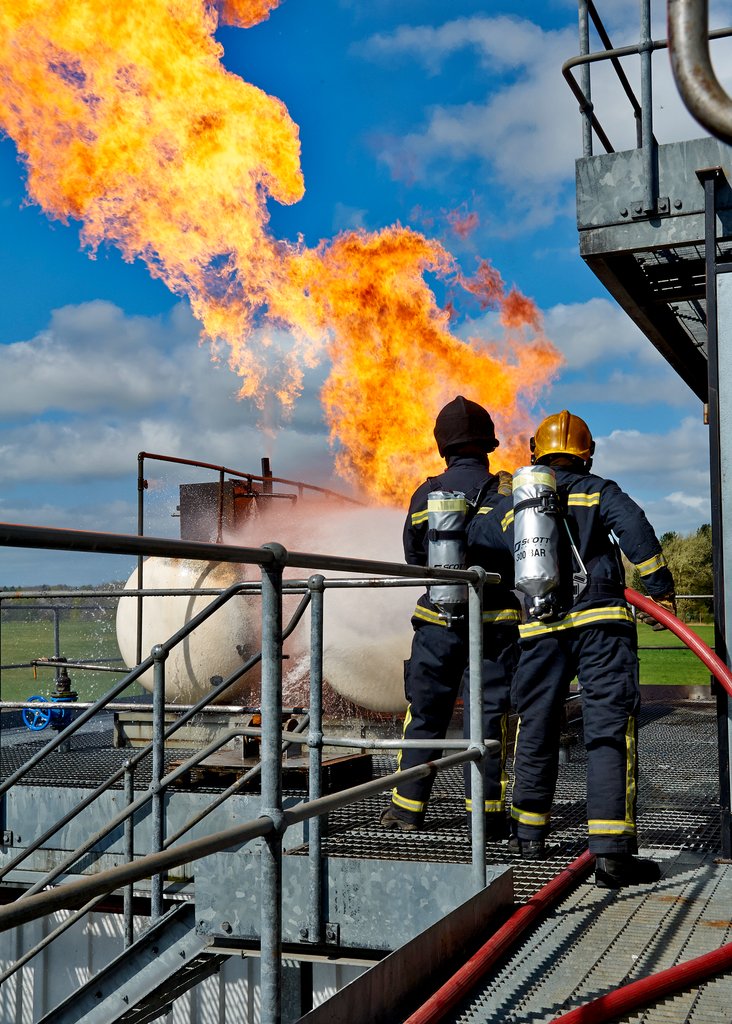 Two firefighters spraying a fire at a tank