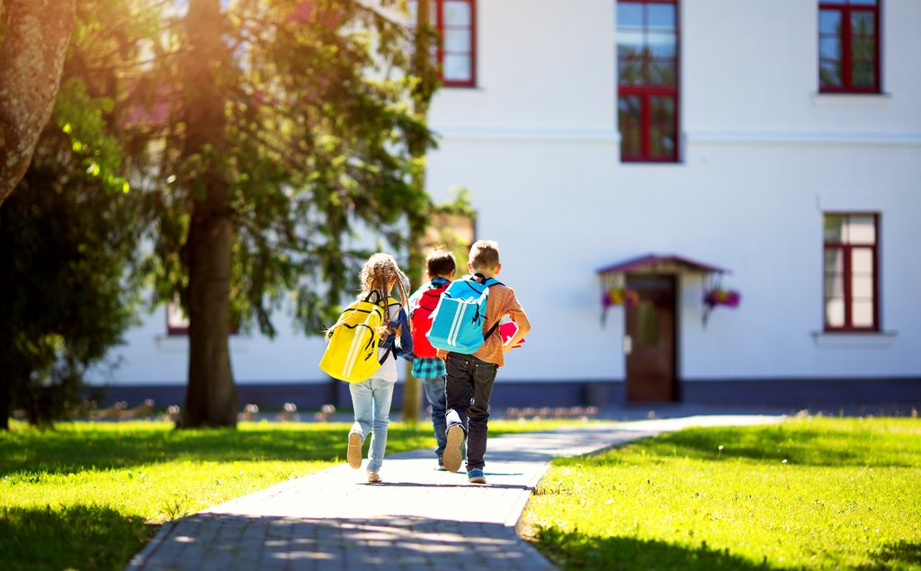 Three young students wearing brightly coloured backpacks, walk into school.