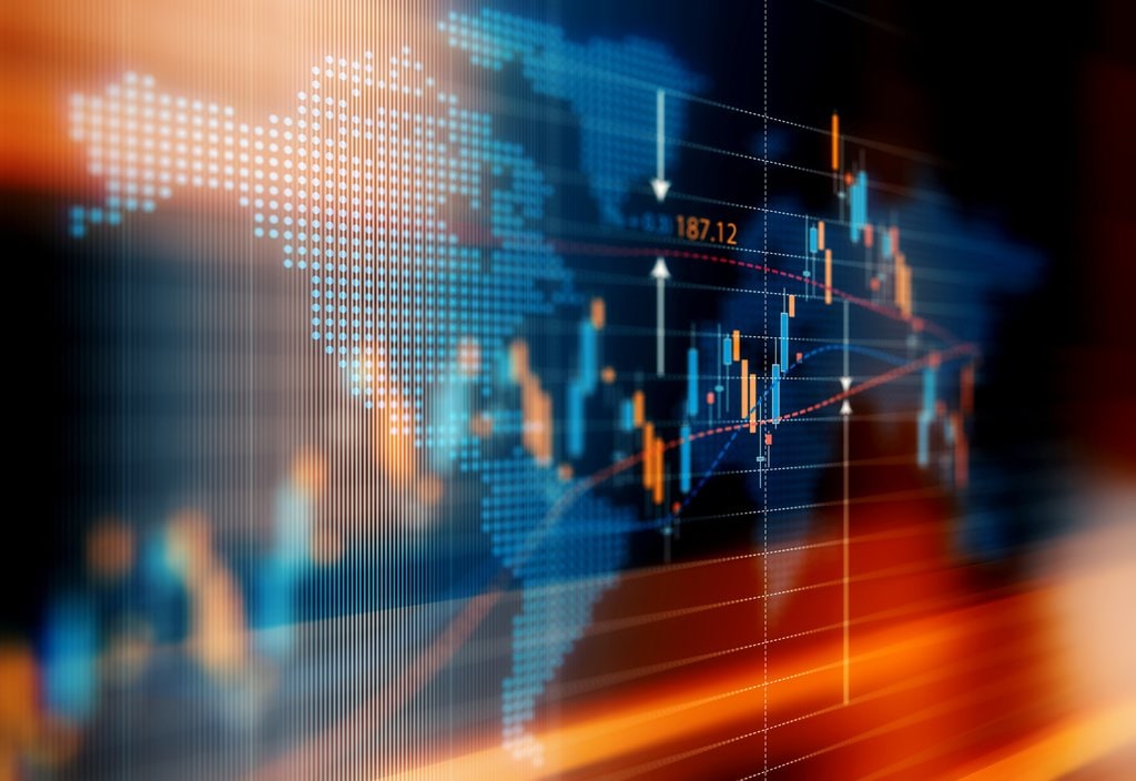 A digital display shows a world map overlaid with financial graphs and data points, including candlestick charts and numerical values, indicating stock market activity.