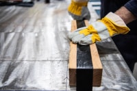 Image of gloved hands binding tape around a wood block on top of covered material