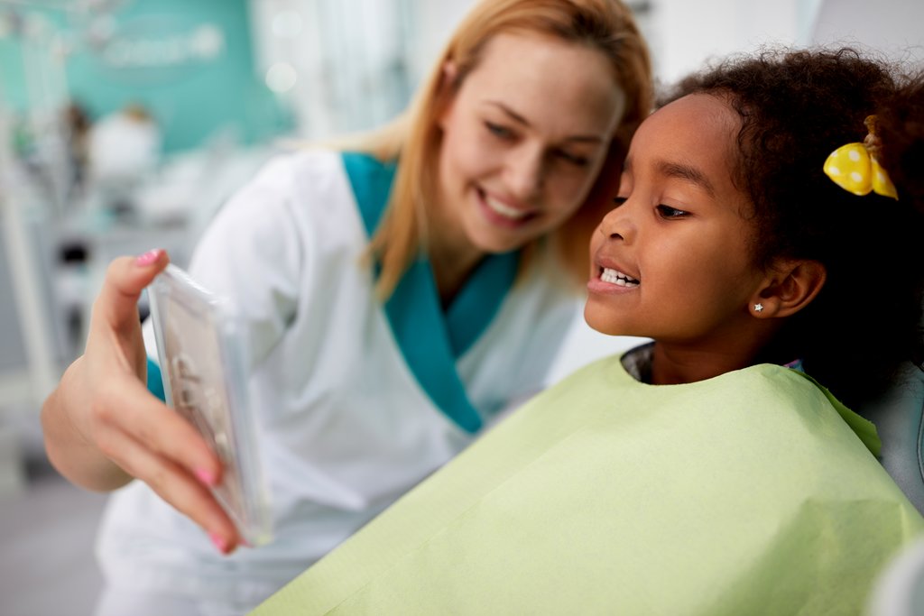 Dentist showing little girl her teeth in mirror.