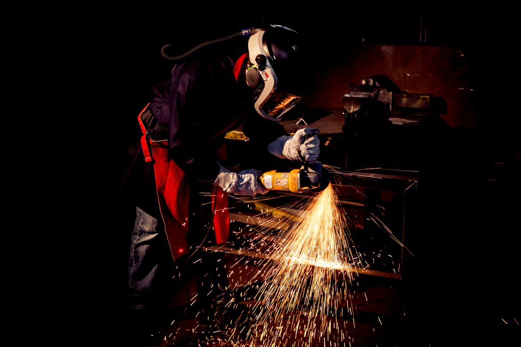 Man wearing protective equipment using abrasive on metal