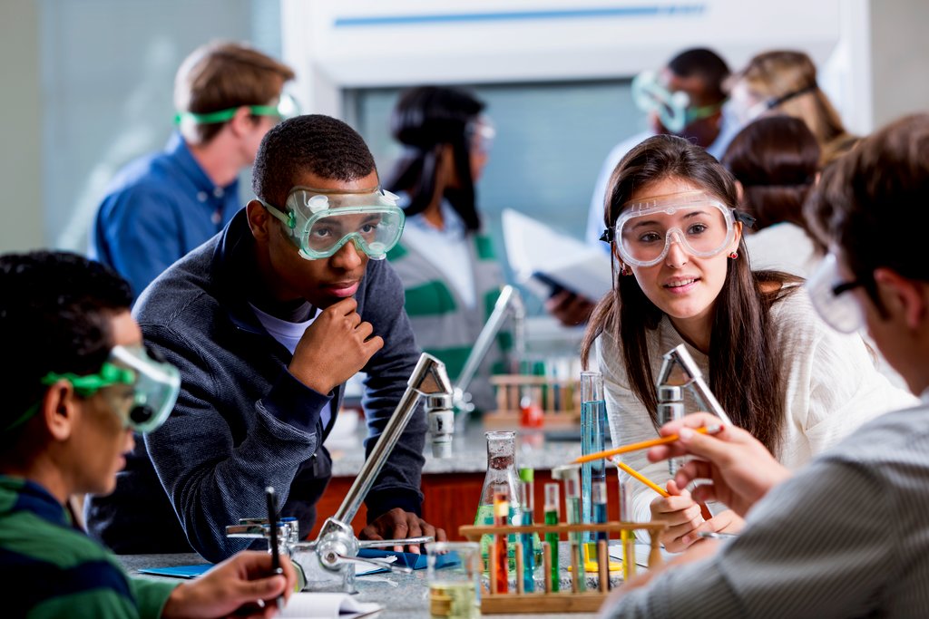 A group of individuals wearing safety goggles are gathered around a laboratory table, engaged in a science experiment.
