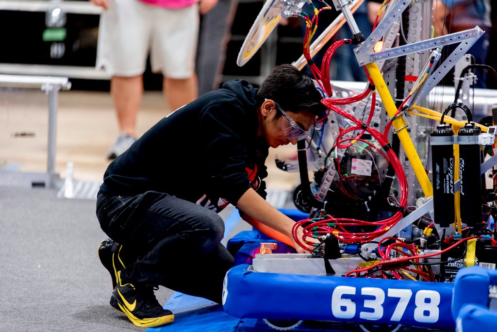 Young male student in a black hoodie working on a robot during a FIRST Robotics competition.