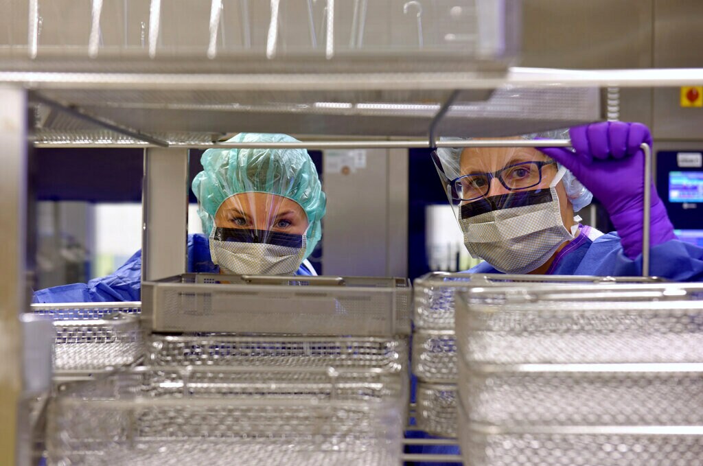 Deux techniciennes de laboratoire/scientifiques examinent une étagère d'échantillons, portant des filets à cheveux, des appareils de protection respiratoire et des écrans faciaux.