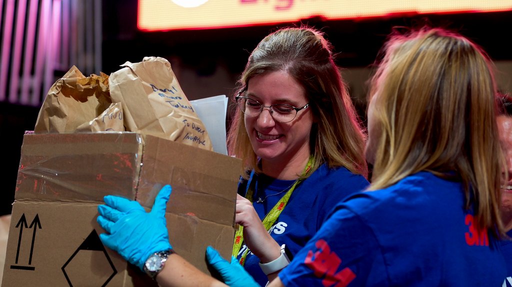 Two 3M volunteers helping each other lift a box