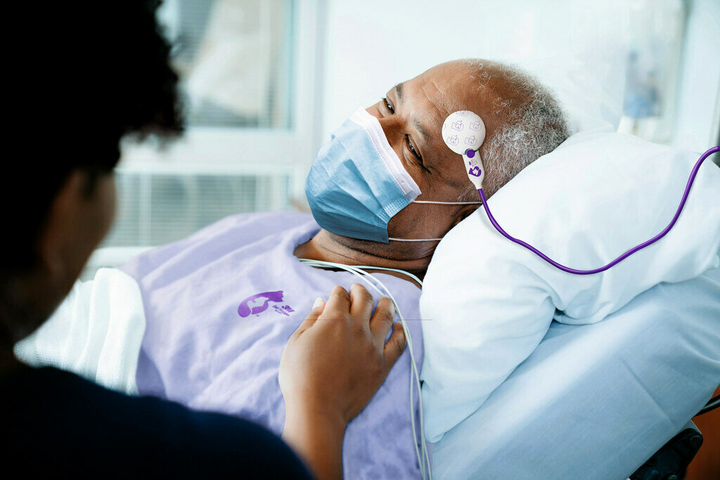 Patient lying in a bed with a temperature monitor on his forehead