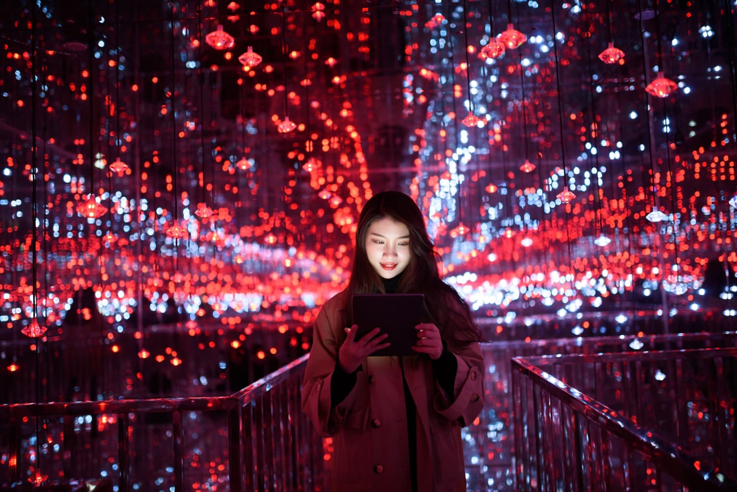 A person holding a tablet stands in front of a vibrant, illuminated background with red and blue lights.