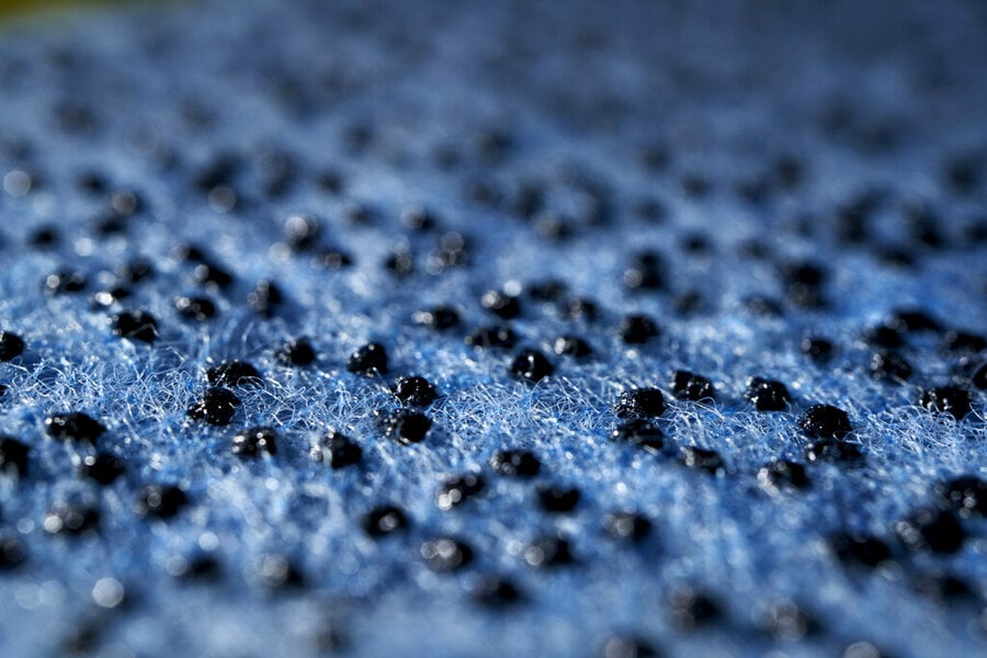 Close-up view of a textured blue surface with small black granules scattered across it.