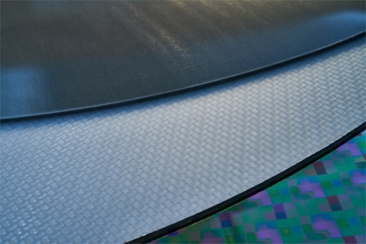 Close-up view of three overlapping semiconductor wafers, each displaying distinct textures and patterns.