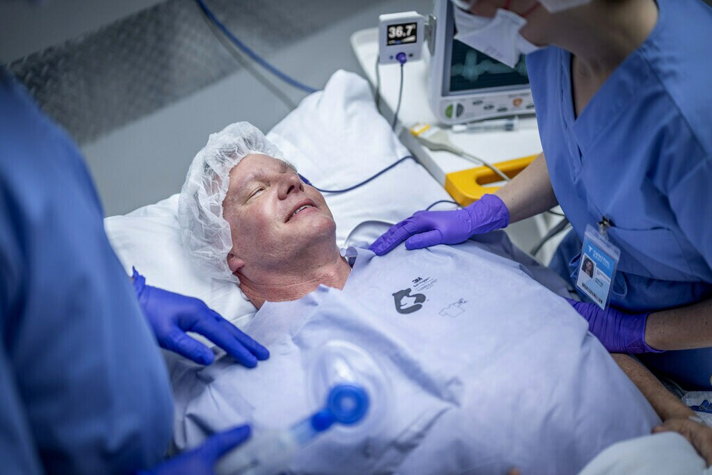 Homme allongé sur un brancard avec un professionnel de la santé posant sa main sur l'épaule du patient