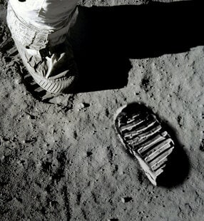 An astronaut boot and a distinct footprint are visible on the lunar surface, highlighting the iconic moment of human exploration on the moon.