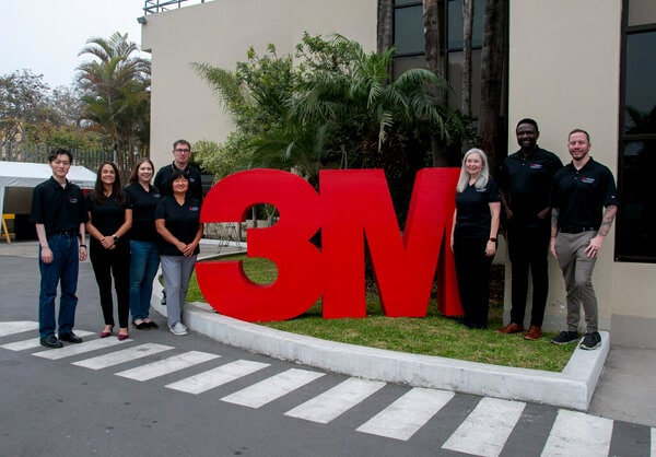 A group of five people standing outdoors next to a large red 3M logo.