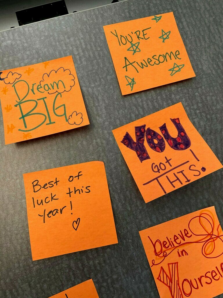 Des feuillets Post-it® orange collés sur une table et portant des messages inspirants écrits au feutre coloré