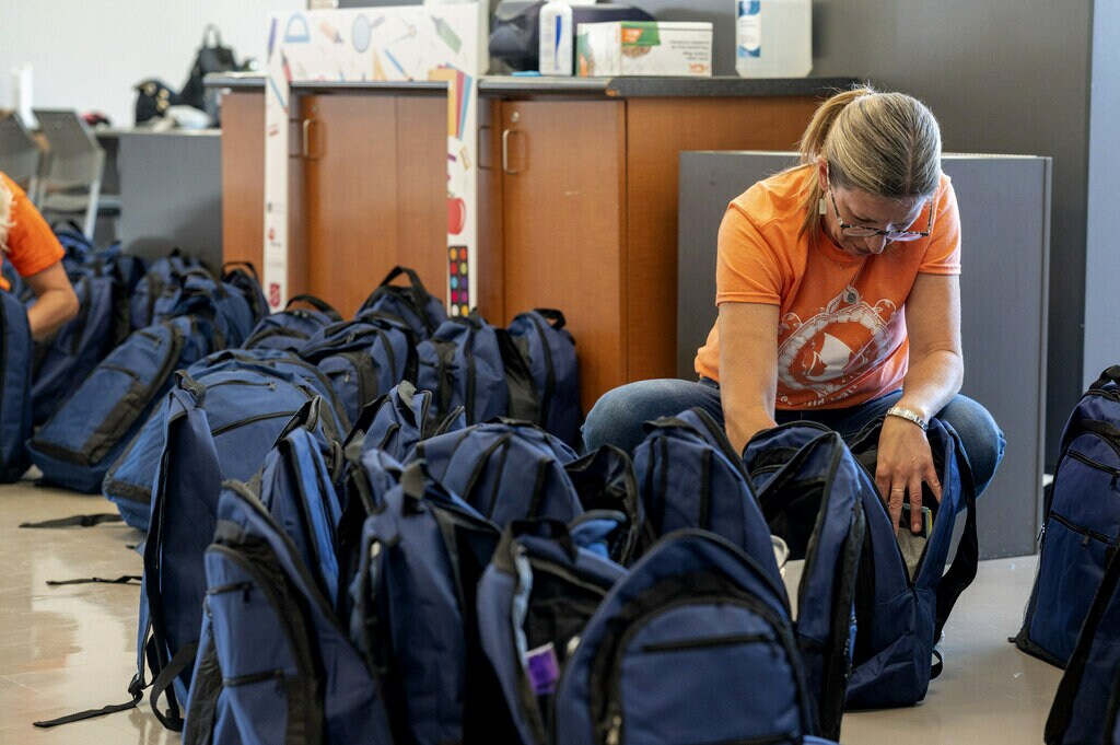 Laura kneels on the ground to fill backpacks with school supplies