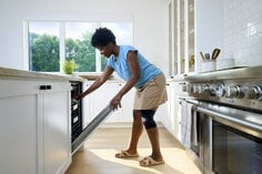 Woman loading dishwasher wearing ACE compression knee support.