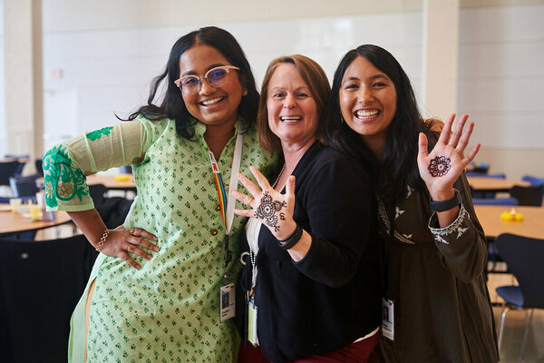 Three individuals stand together, displaying intricate henna designs on their hands.