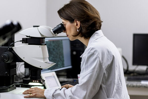 A scientist or researcher in a white lab coat is using a microscope to examine a sample.