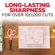 Scotch Precision Ultra Edge Scissors have long-lasting sharpness for over 100,000 cuts.  Image shows a gift wrapped with a pair of pink and white handled scissors on a table.