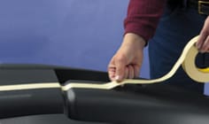 A worker applies masking tape to an irregularly shaped surface