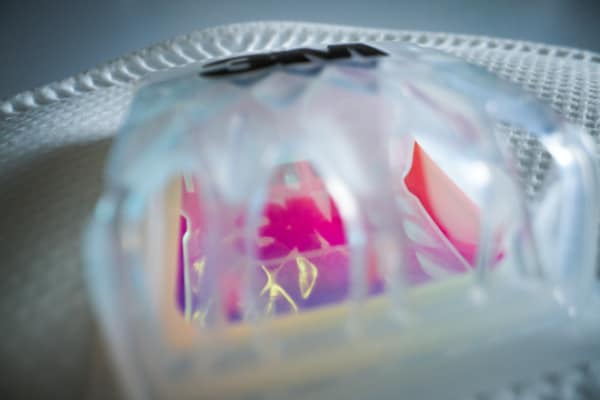 A close-up view of a translucent, iridescent object with a geometric design, casting colorful reflections and shadows on a textured white surface.