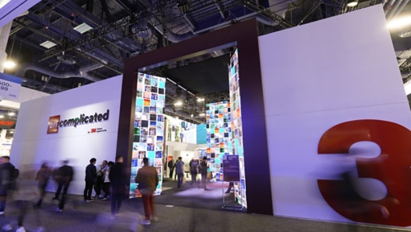 An exhibition booth with a large, illuminated entrance made of colorful panels, featuring the 3M logo and the word complicated on the wall.