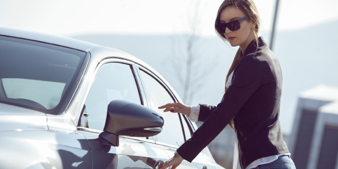 An individual with sunglasses opening the driver's side door on a sunny day.

