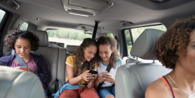 Interior view of a vehicle with kids in the back seat looking at their phones.
