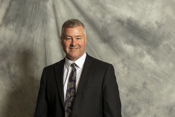 Portrait of Eric Nelson against gray textured cloth background.