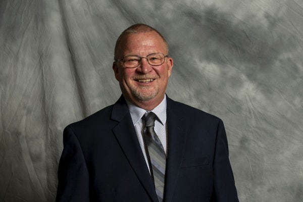 Portrait of Jeffrey O. Emslander against gray textured cloth background.
