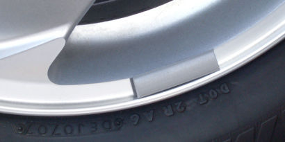 Close up of a grey tire balance weight adhered to the wheel.