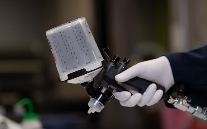 Close-up of an air-powered spray gun used for applying surface pre-treatment.