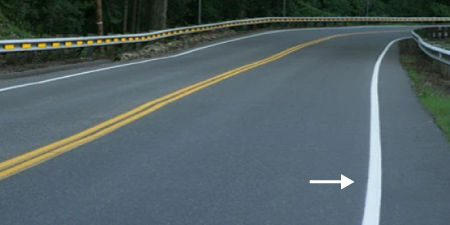 Winding road on a dry day, a bright reflective white road line is highlighted.