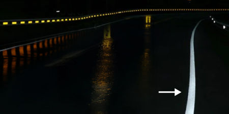 Winding road at night during the rain, a bright reflective white road line is highlighted.