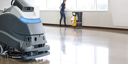 An employee cleaning a large lobby space with an autoscrubber.
