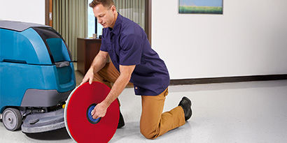 An individual changing out the floor pad in an autoscrubber.