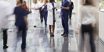 A busy hospital hallway with many people walking on its shiny floors.