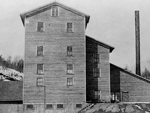 A historic, multi-story wooden building with several windows, situated on a sloped terrain.